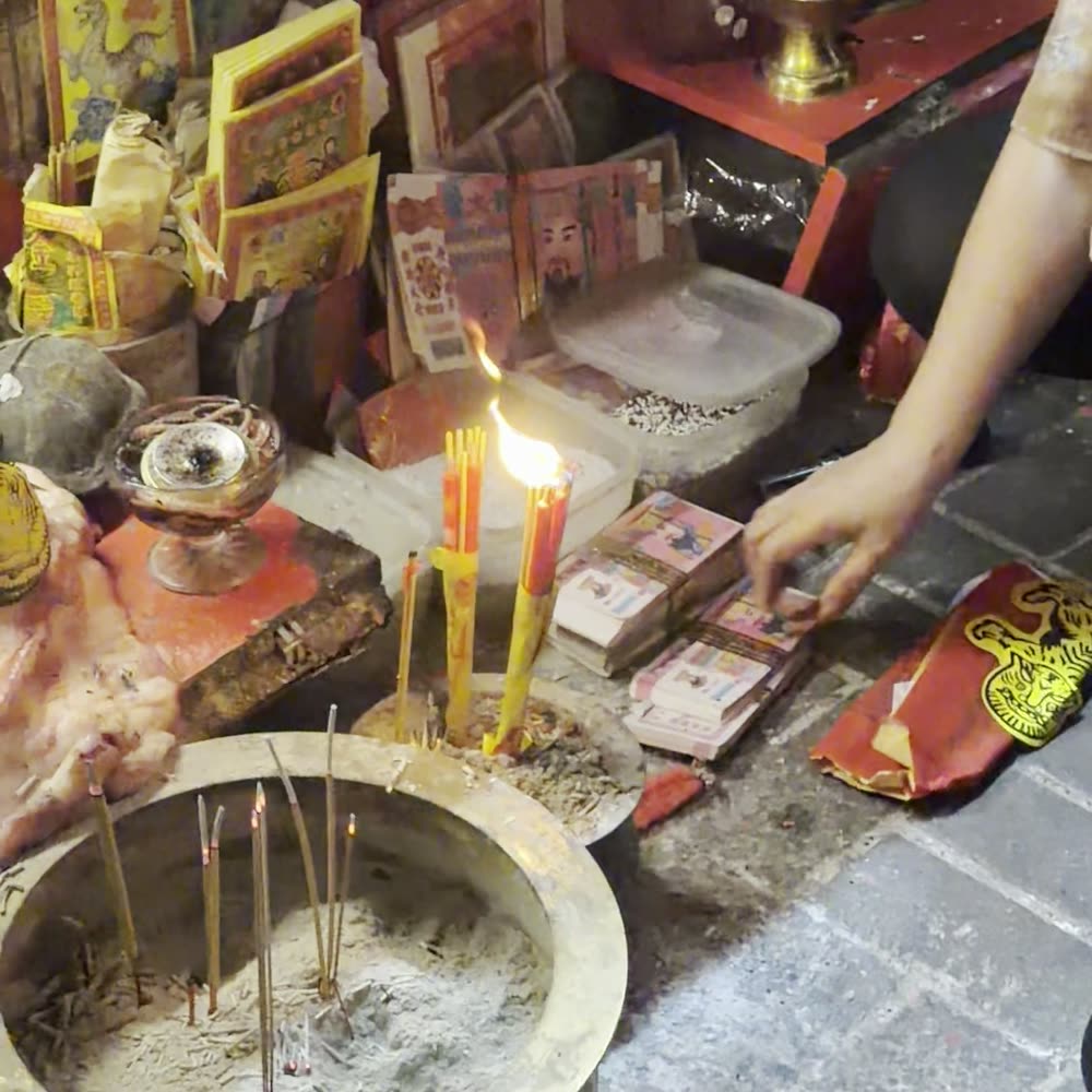 The ash bowl at the stall: incense sticks planted in the ash, candles burning beside it